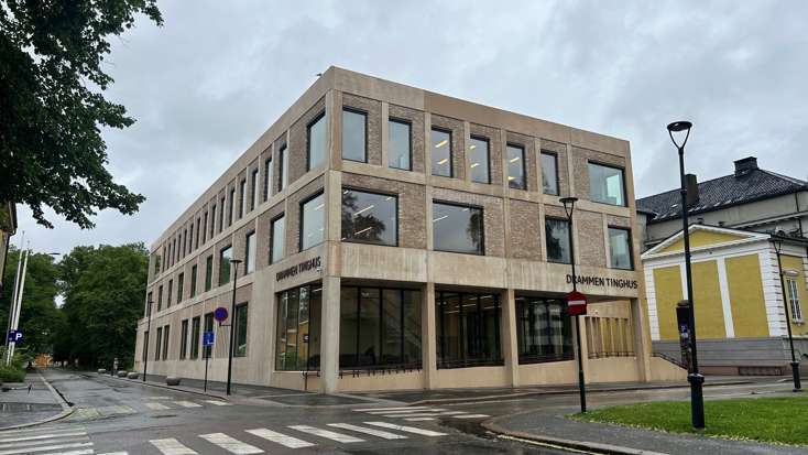 Drammen tinghus sett fra hjørnet på motsatt side i et veikryss. Bygningen er i lys betong og mur og er i to etasjer.