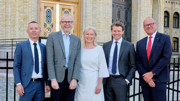 Fem personer står foran porten til Stortinget og smiler til kamera.