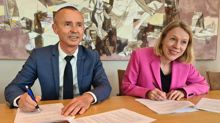 Bilde av Domstoladministrasjonens direktør Sven Marius Urke og utenriksminister Anniken Huitfeldt som sitter ved et bord og signerer avtalen. Foto: Domstoladministrasjonen