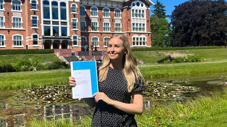 Bilde av Christina Bruun Floan som stolt holder opp masteroppgaven sin.