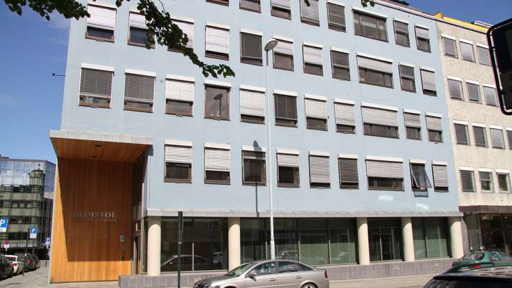 Høyt lyst betongbygg i seks etasjer, med høyt inngangsparti på venstre hjørne som går over to etasjer.